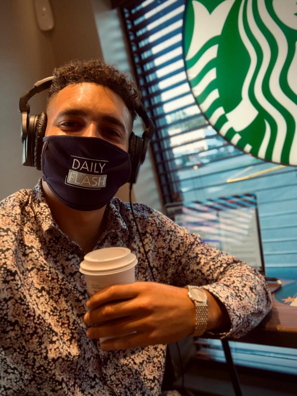 a man wearing headphones and a face mask holding a coffee cup