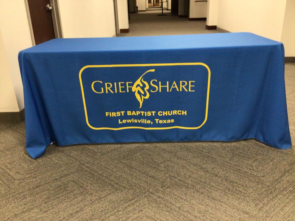 Customer photo from Kermit of our Serged Open-Back Polyester Table Throw - 6', a blue table cloth with yellow writing on it