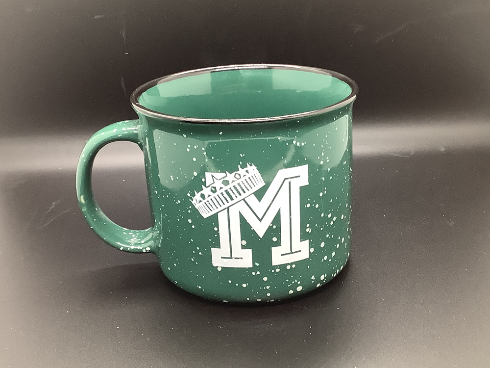 Customer photo from Keia of our Campfire Ceramic Mug - Colors - 15 oz., a green mug with a letter m on it