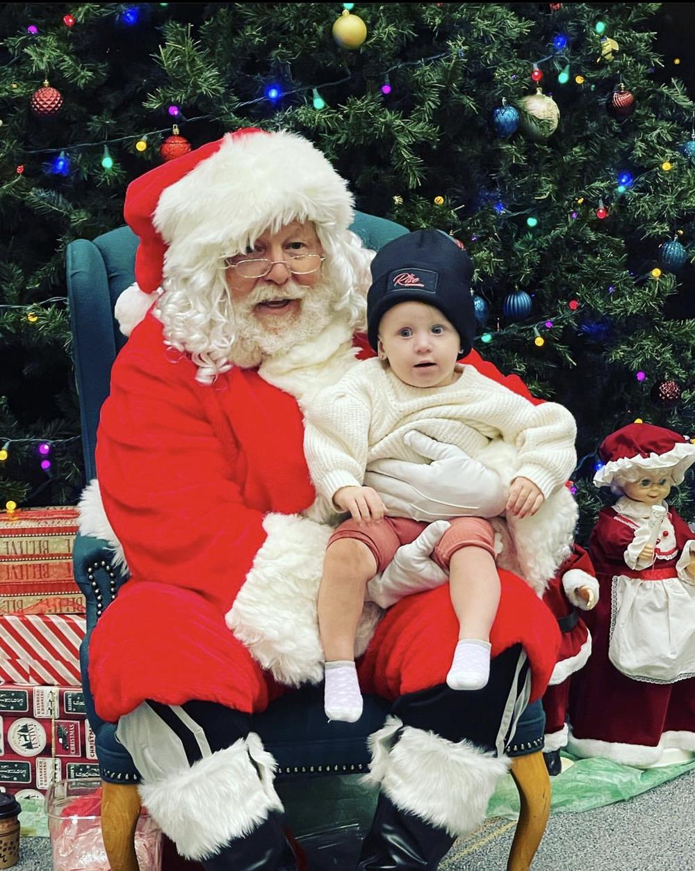 Customer photo from Rian of our Cuffed Knit Beanie with Patch, a man in a santa garment holding a baby