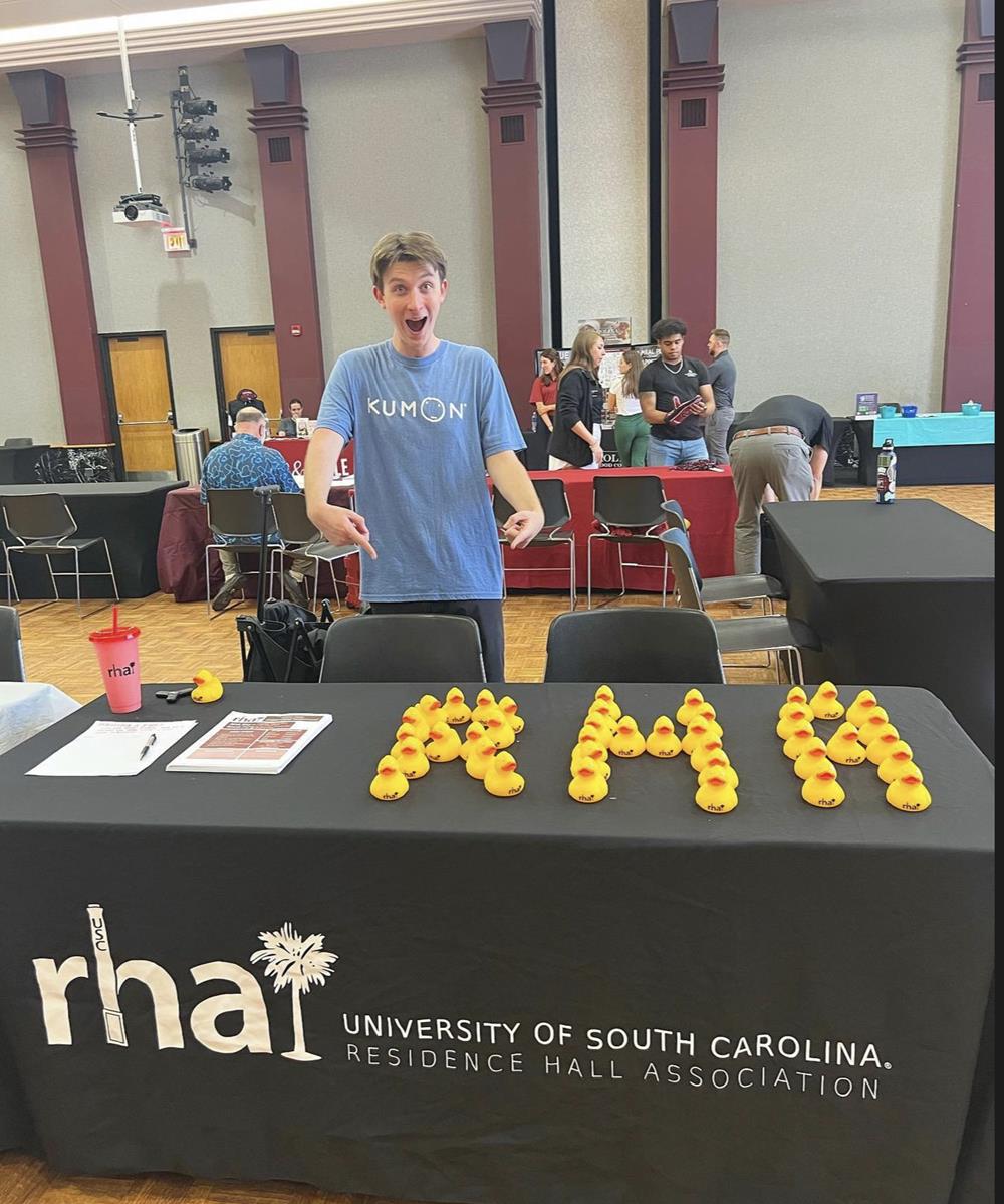 Customer photo from Will of our Rubber Duck - Medium, a man standing in front of a table with yellow letters on it
