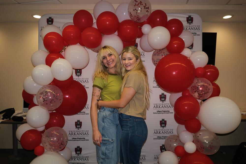 two women standing in front of a red and white balloon arch