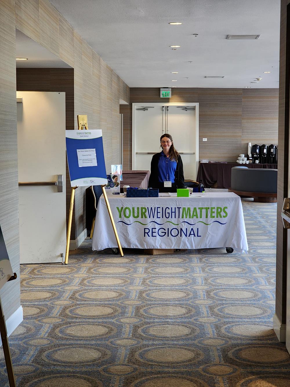 Customer photo from Michelle of our Serged Closed-Back Table Throw - 6', a woman standing behind a table with a sign