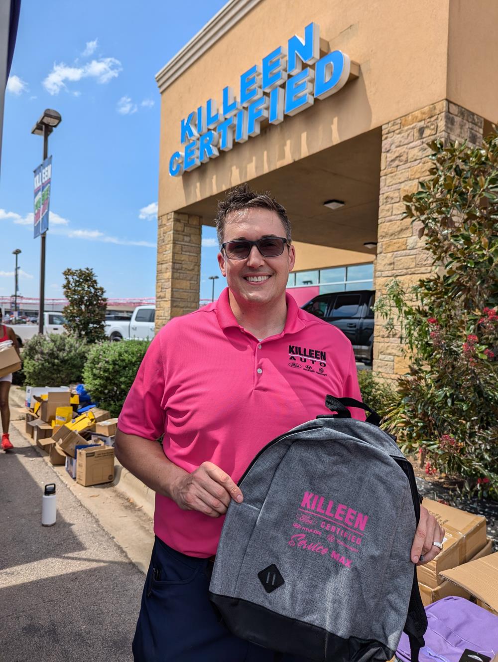 a man in a pink shirt holding a backpack in front of a building