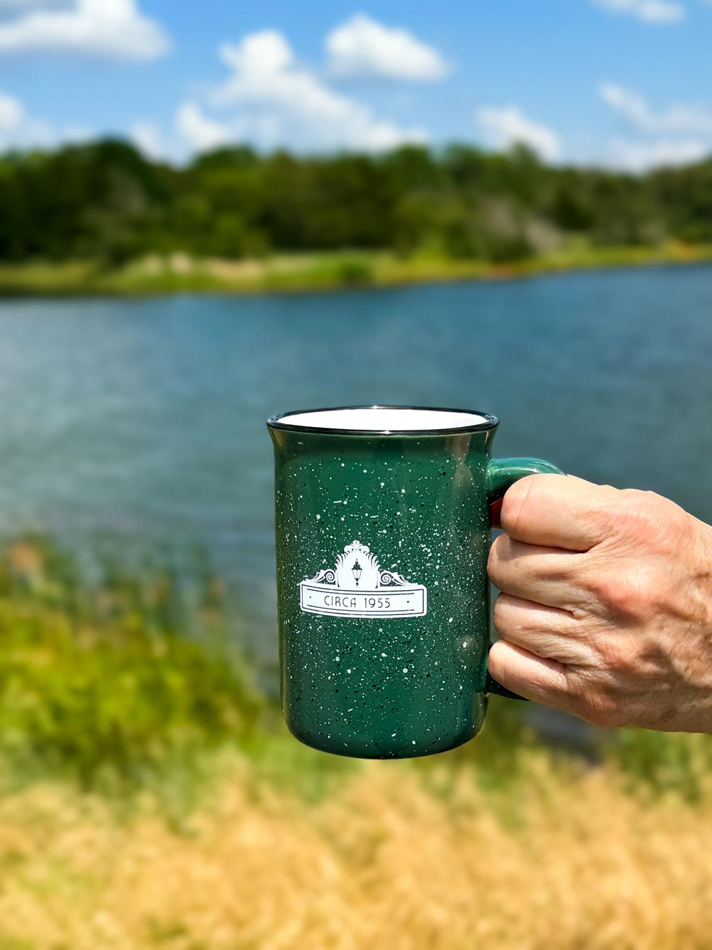 Customer photo from Nicole of our Tall Campfire Mug - 12 oz, a hand holding a green mug with a white logo on it