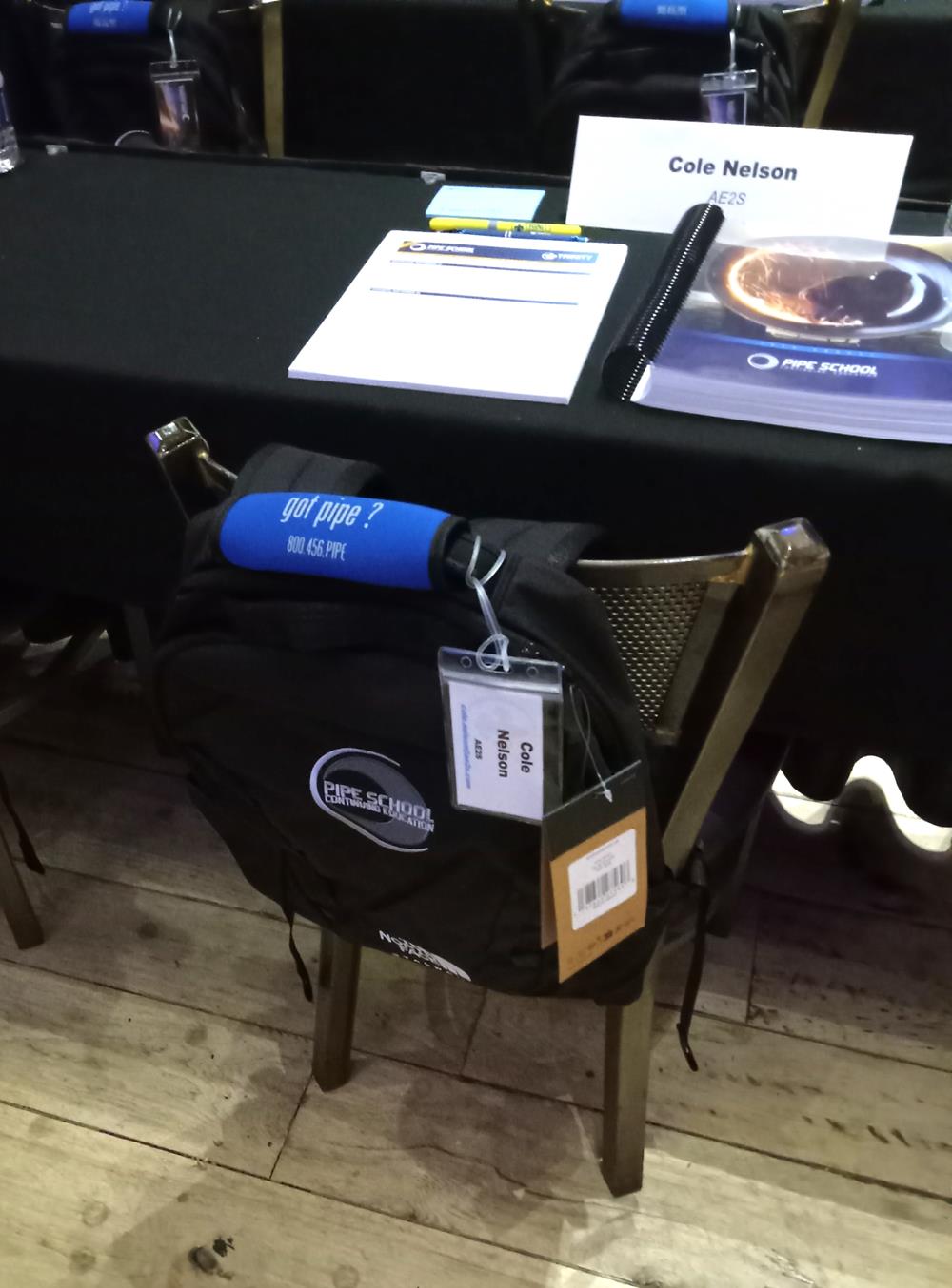 Customer photo from Kristy of our Grip-it Luggage Identifier, a black backpack on a chair with a table and a book