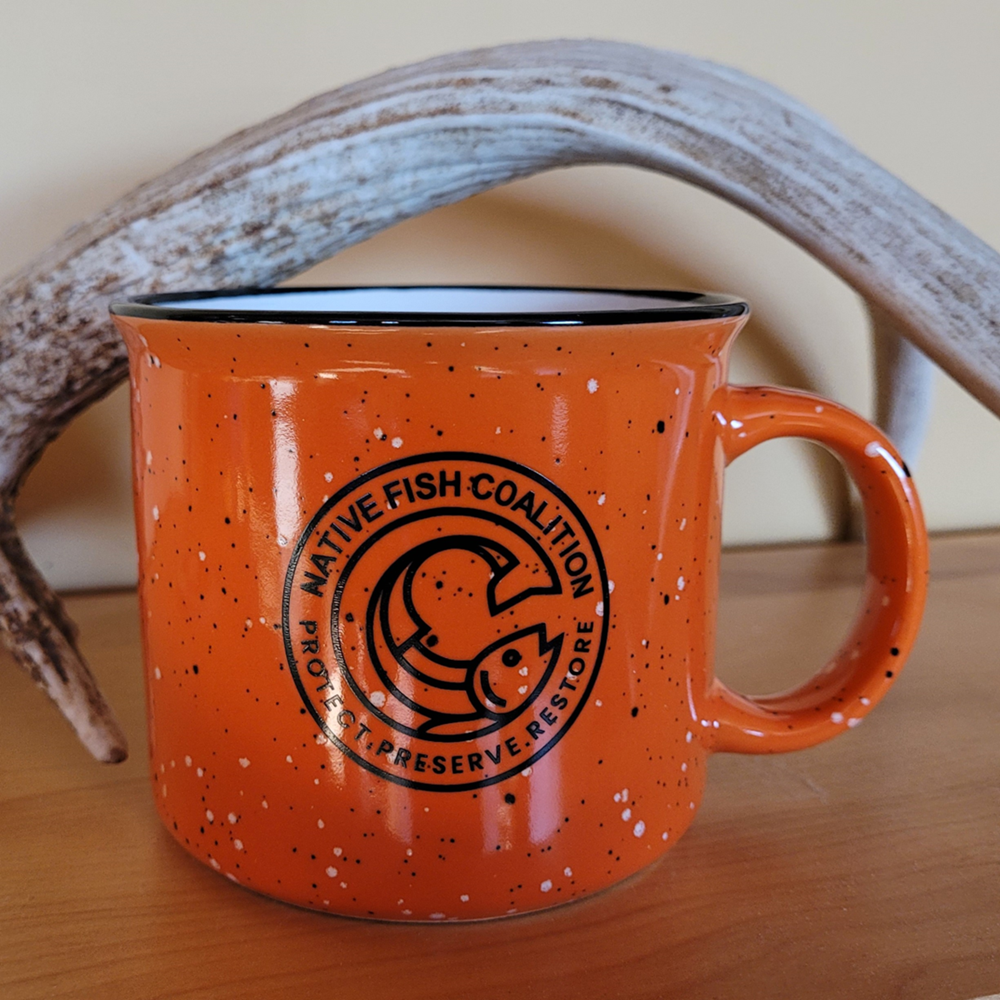 an orange mug with a black design on it next to a antler