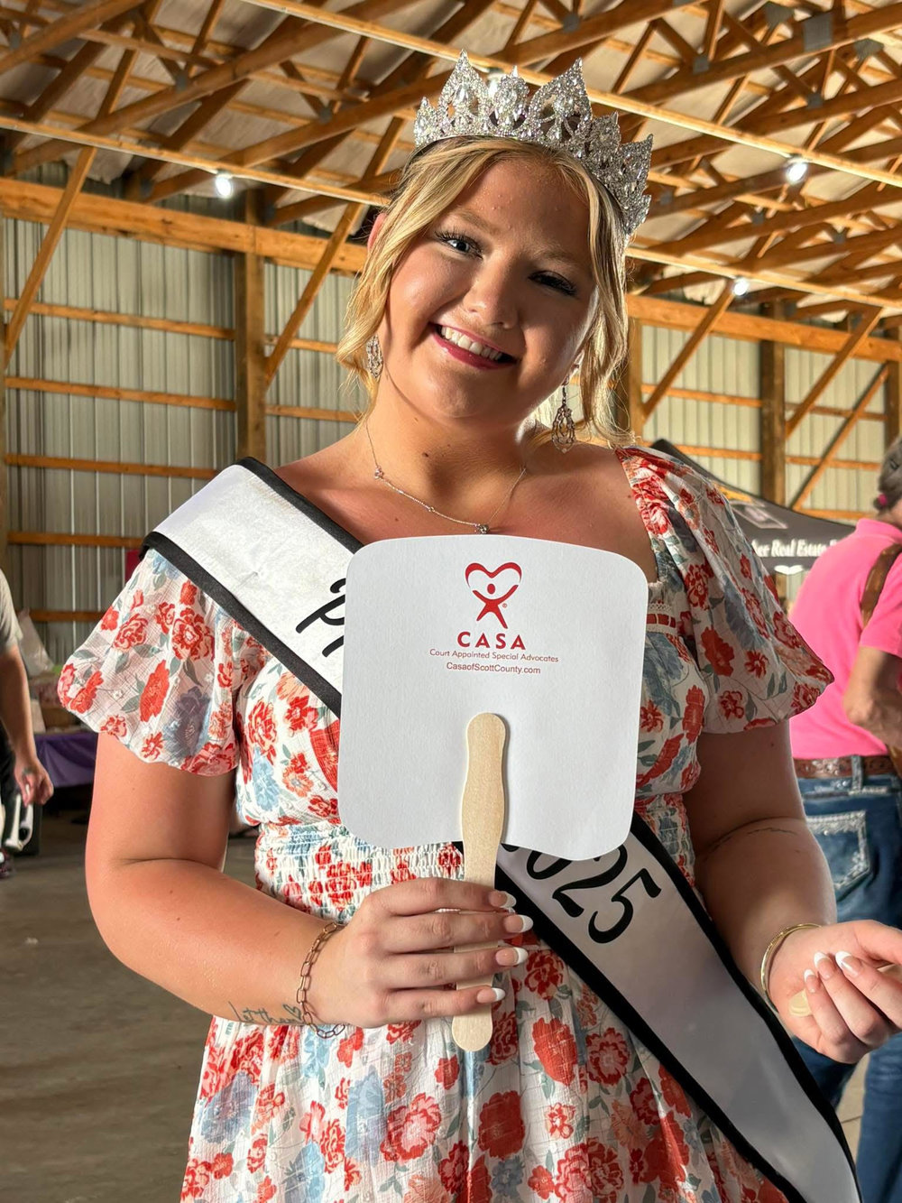 Customer photo from Kenneth of our Hand Fan - Slice, a woman wearing a crown and sash holding a fan