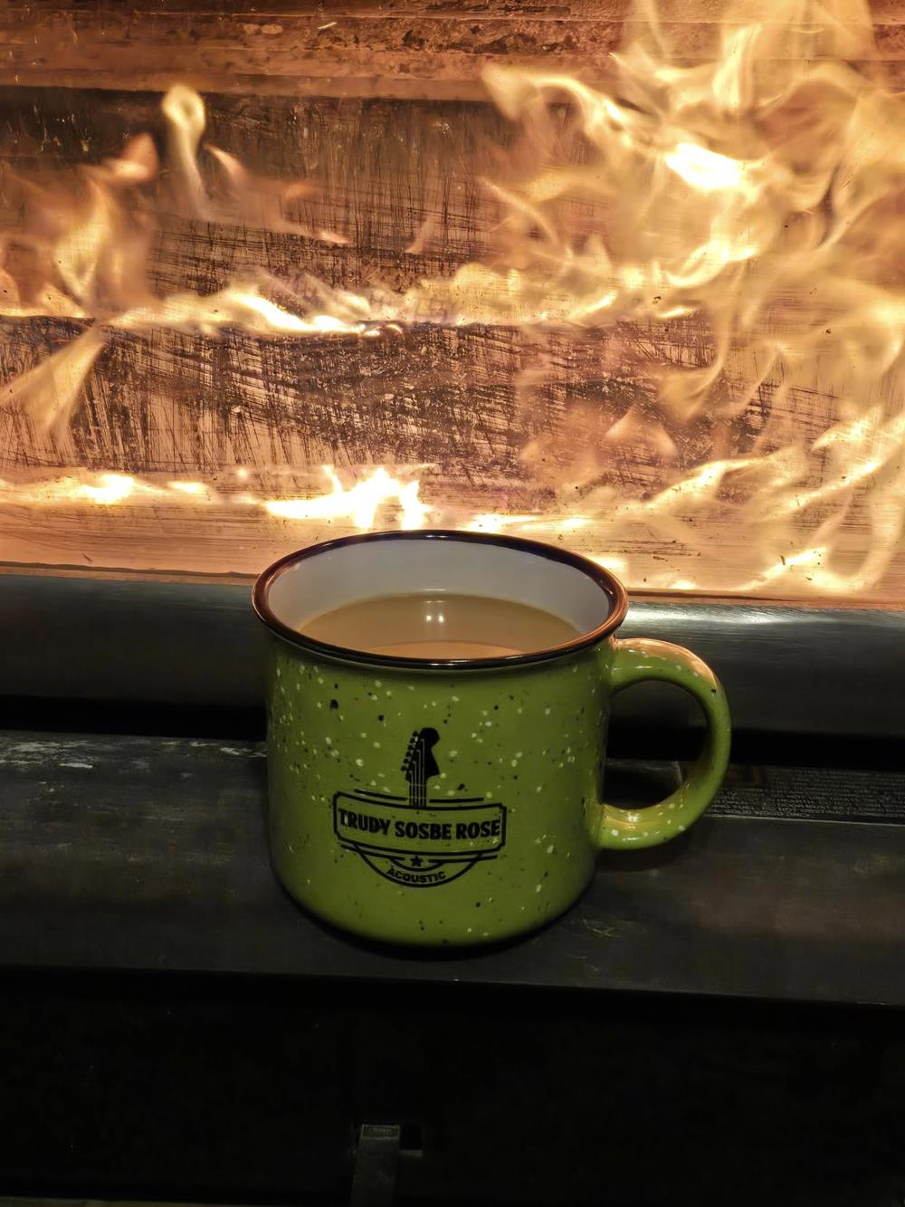 Customer photo from Darrell of our Campfire Ceramic Mug - Colors - 15 oz., a mug of coffee in front of a fire
