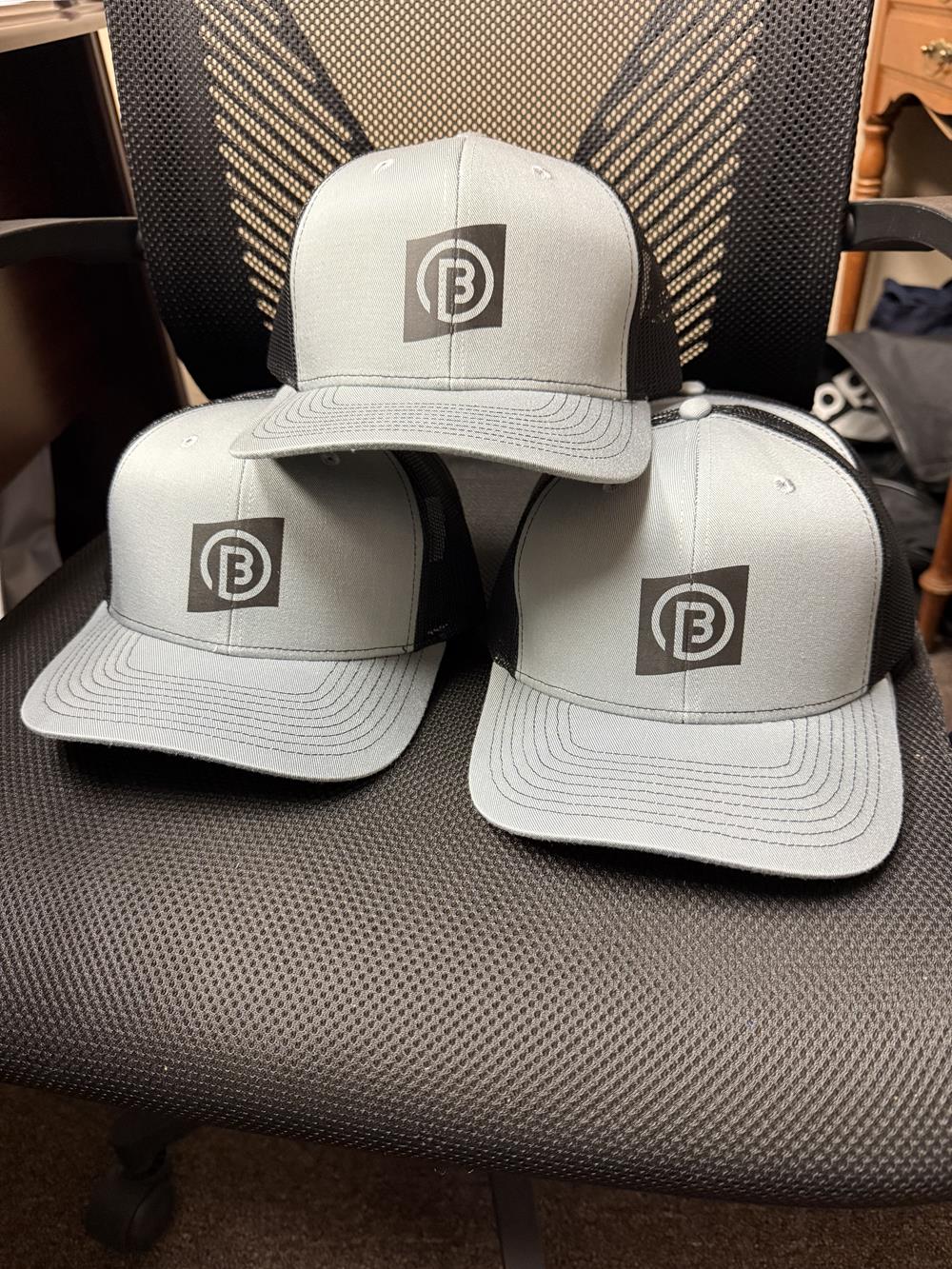 Customer photo from Ian of our Crofton Snapback Trucker Cap, a group of hats on a chair