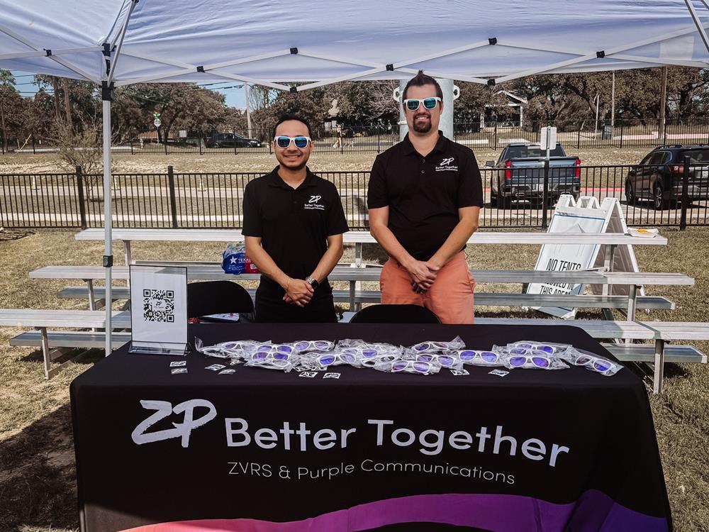 Customer photo from Marketing of our Light-Up Foam Cheer Stick, two men standing next to a table with a table with purple and white text