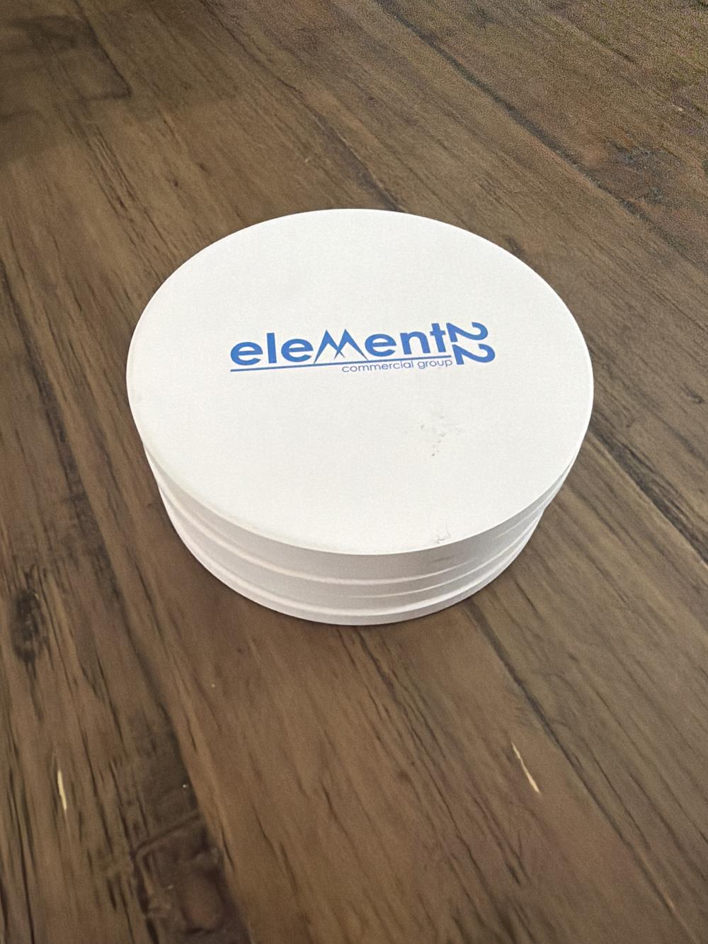Customer photo from Kenny of our Absorbent Stone Coaster - Round, a stack of white coasters on a wood surface
