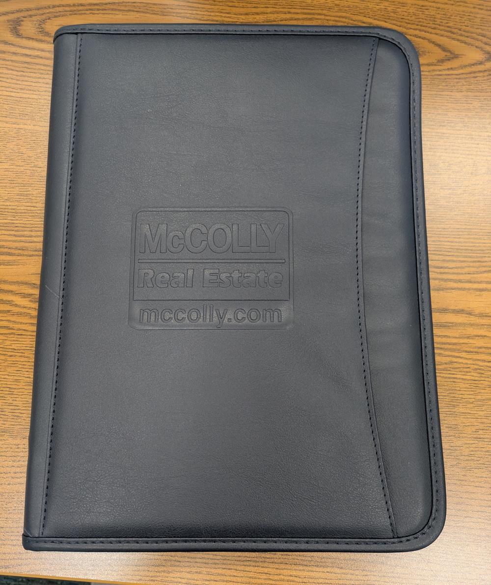 Customer photo from Sharon of our Zippered Vinyl Portfolio - Debossed, a black leather folder on a wood surface