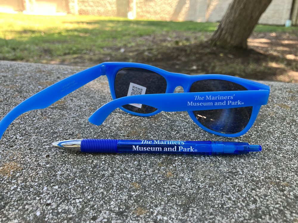 Customer photo from Ann of our Sunglasses, a blue sunglasses and a pen on a concrete surface