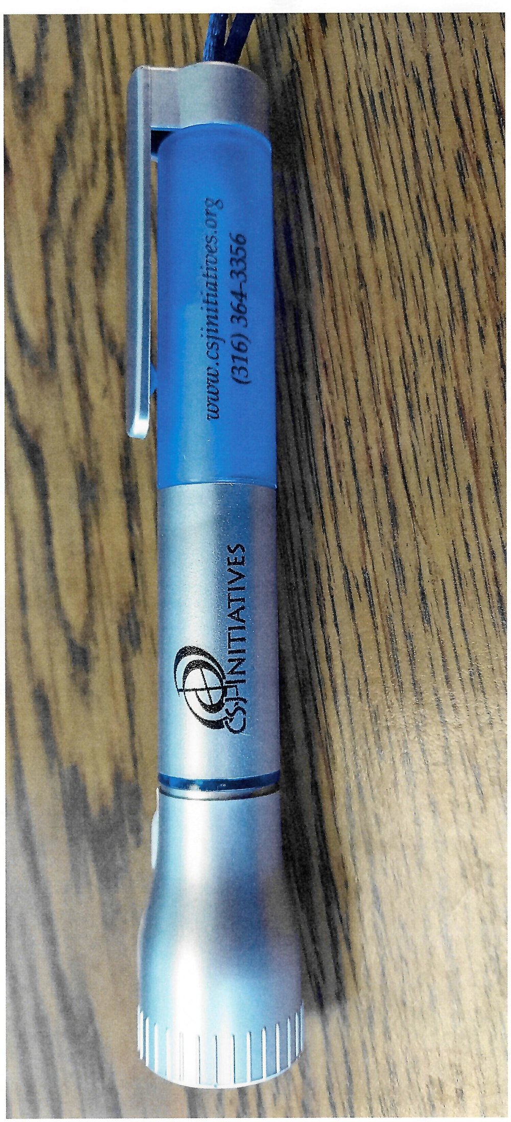 Customer photo from Katrina of our Flashlight with Pen and Lanyard, a blue pen on a wood surface