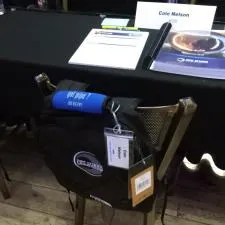 Customer photo from Kristy of our Grip-it Luggage Identifier, a black backpack on a chair with a table and a book