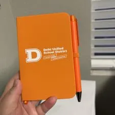 a hand holding an orange notebook and pen