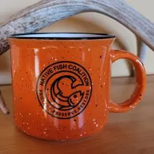 an orange mug with a black design on it next to a antler