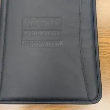 Customer photo from Sharon of our Zippered Vinyl Portfolio - Debossed, a black leather folder on a wood surface