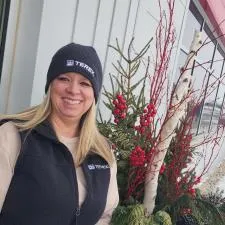 Customer photo from Debi of our New Era Fleece Lined Beanie, a woman smiling next to a plant