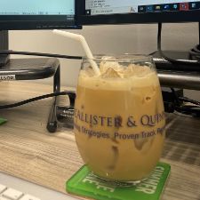 a glass of brown liquid with a straw in front of a computer monitor